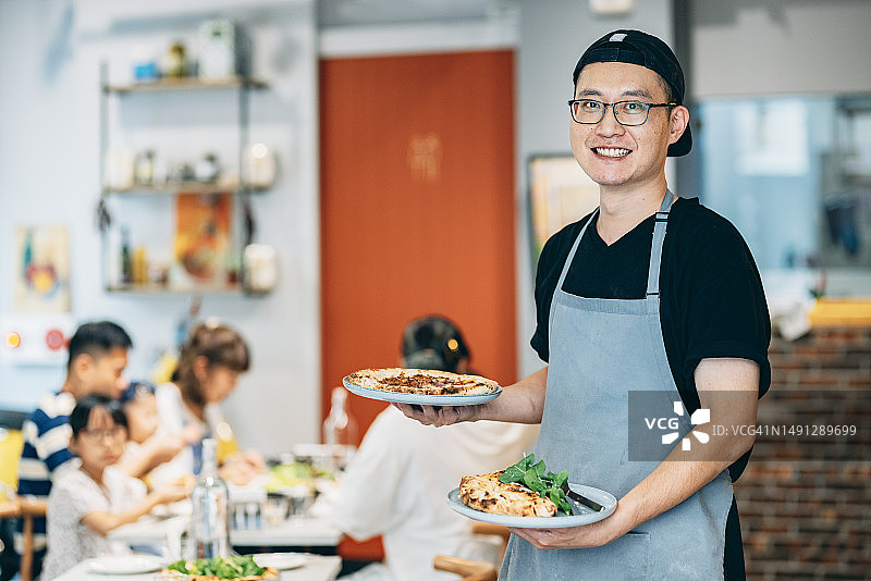 亚洲厨师自信地展示烹饪的食物，对着镜头微笑图片素材