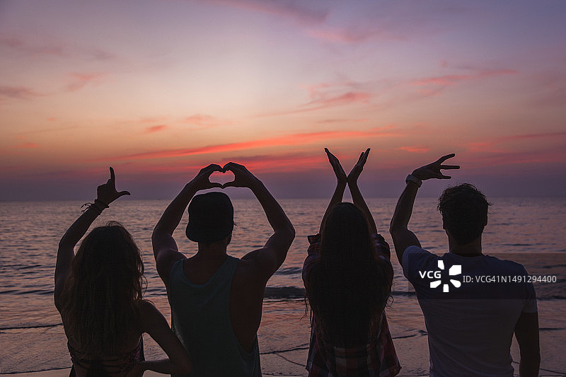 朋友们在日落时分的海滩上手牵手，表达爱意图片素材
