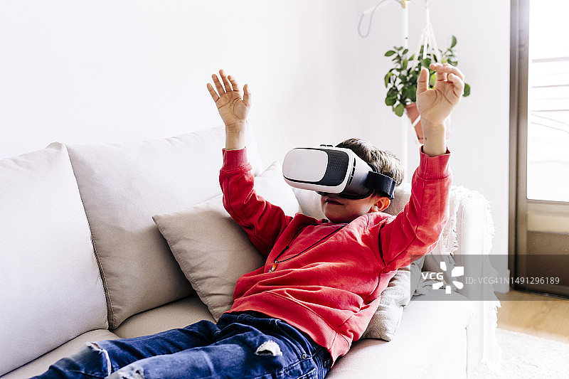 戴着VR头显躺在沙发上举起双臂的男孩图片素材