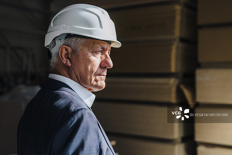 在木工工厂戴着安全帽的沉思的老年商人图片素材