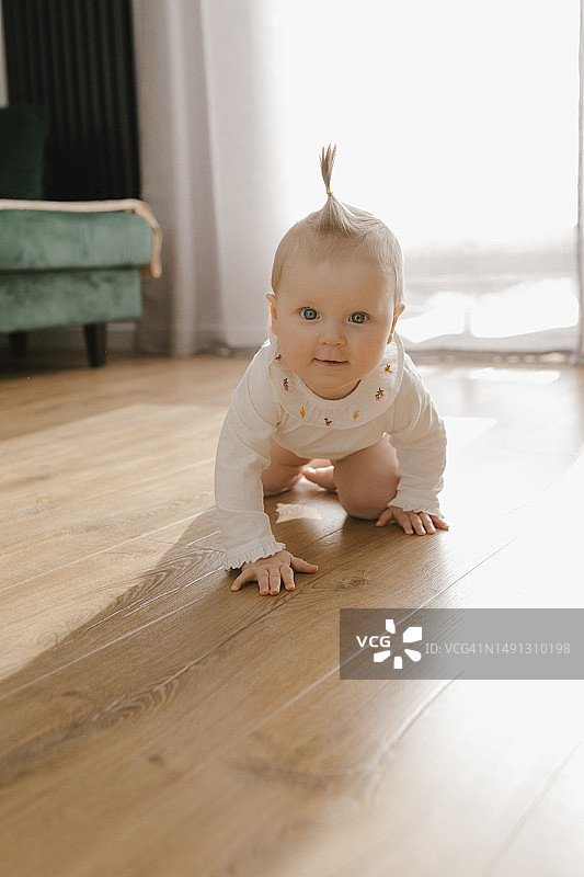 可爱的女婴在家中硬木地板上爬行图片素材