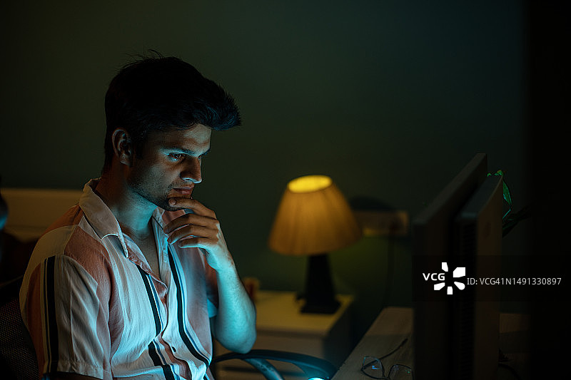 晚上在家办公，在电脑前工作的年轻男人图片素材