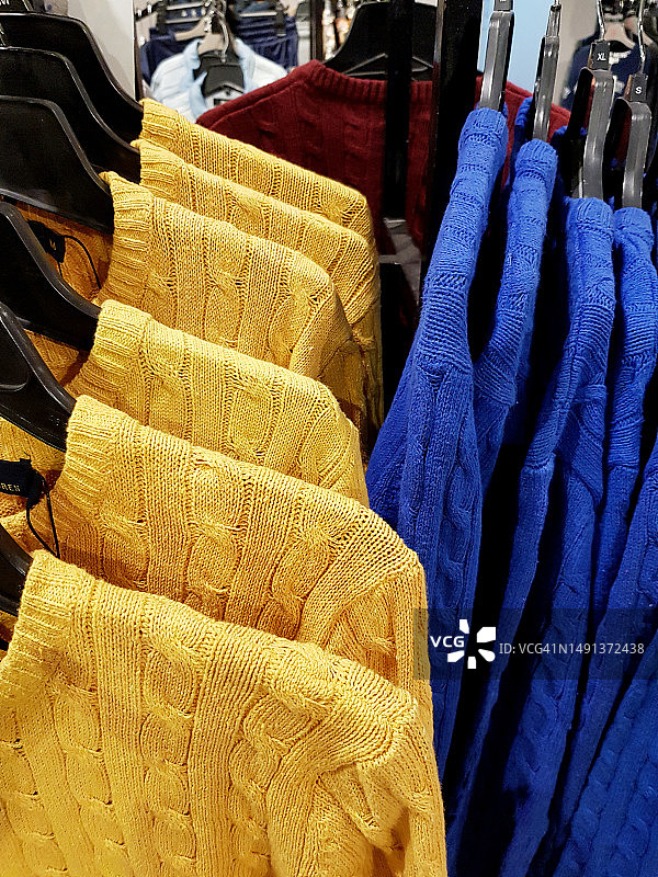 一排蓝黄色针织毛衣挂在衣架上出售图片素材