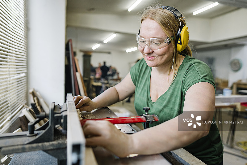 金发女木匠在她的木材作坊里使用圆锯图片素材