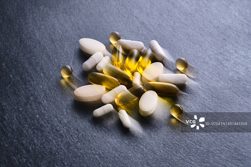 深色桌面上模糊的药丸、维生素和膳食补充剂照片图片素材