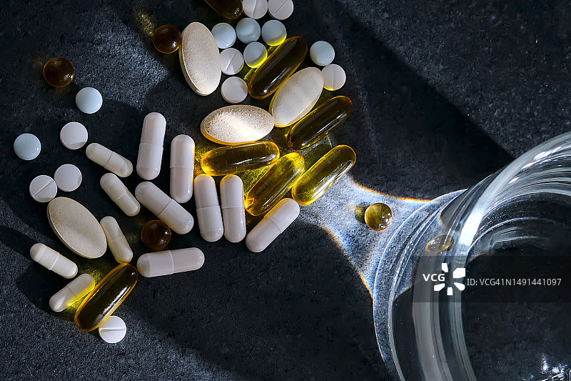 深色桌子上玻璃杯旁边的药片、维生素和膳食补充剂图片素材