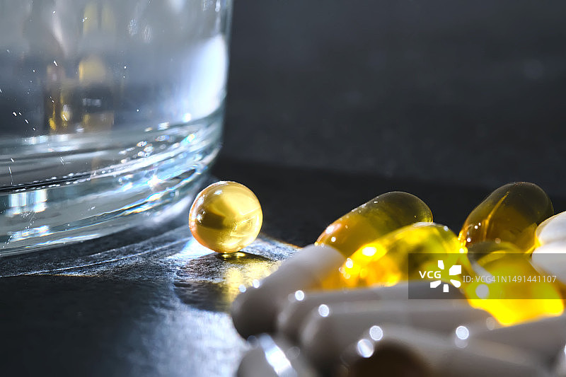 深色桌子上玻璃杯旁边的药片、维生素和膳食补充剂图片素材