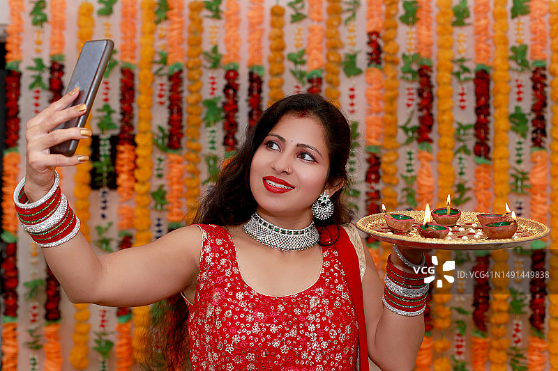 年轻的印度女性在花卉背景下用智能手机自拍图片素材