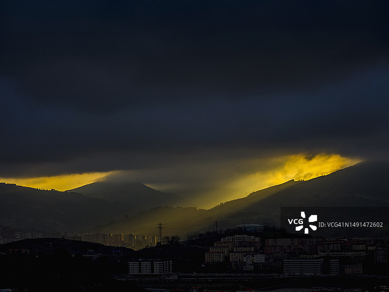 山脉上居民建筑的剪影，有乌云和阳光图片素材