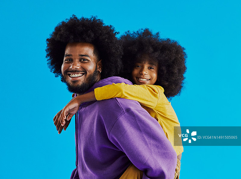年轻的黑人男子背着一个同样发型的黑人小男孩，对着镜头微笑，留有文案空间图片素材