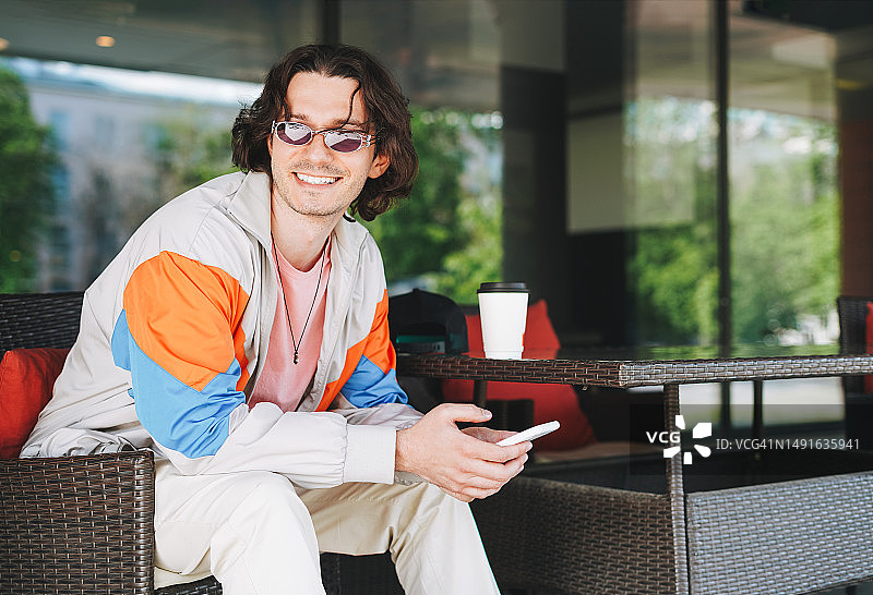 在城市街边咖啡馆使用手机的微笑时尚青年男子肖像图片素材