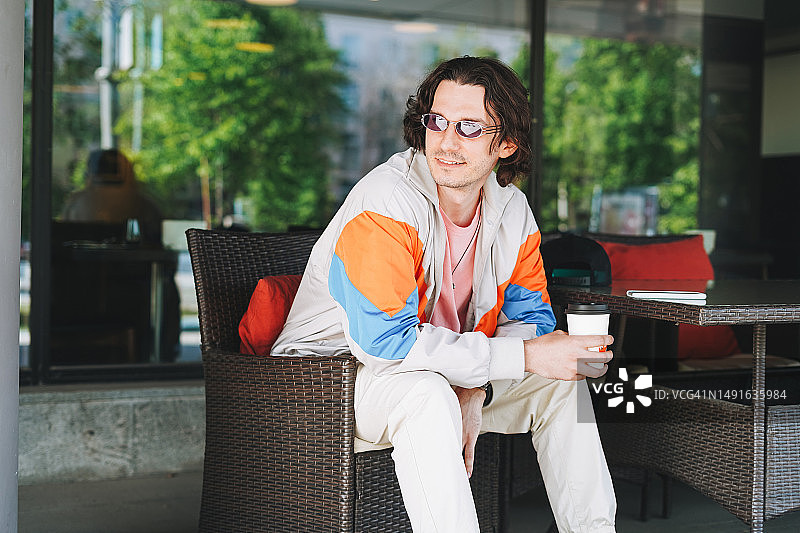 阳光下在街边咖啡馆喝咖啡的年轻男子图片素材