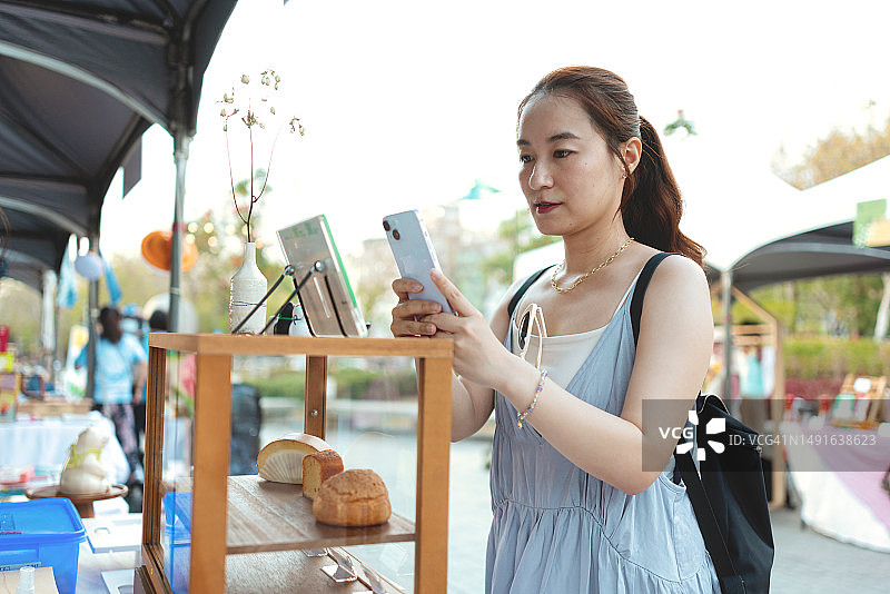 亚洲女性在当地市场观光，用手机上的二维码支付图片素材