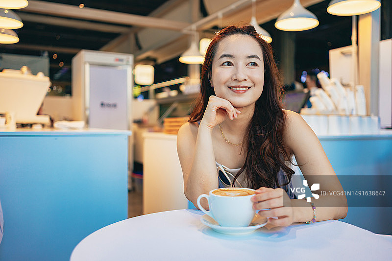 亚洲女性在旅游目的地寻找自己喜欢的咖啡馆，一边品尝咖啡，一边欣赏窗外美丽的景色图片素材