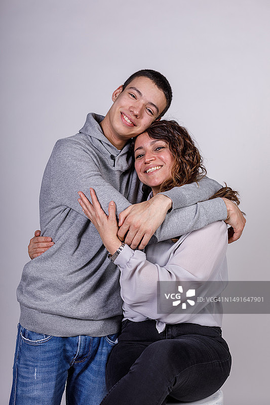 快乐的青少年男孩和他的母亲站在白色背景前，拥抱和联结图片素材