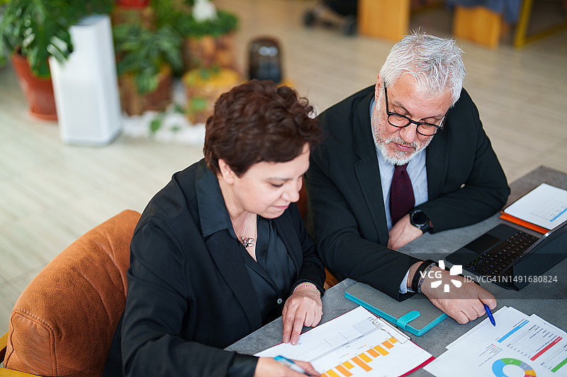 在餐厅使用便携设备和文件的商务人士图片素材