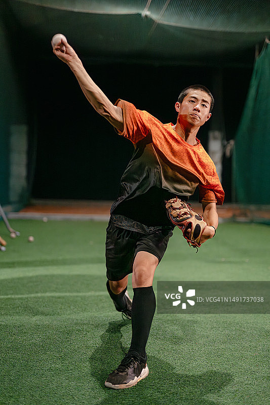 棒球投手在夜间棒球练习中向击球笼中的捕手投掷快速球的自我训练图片素材