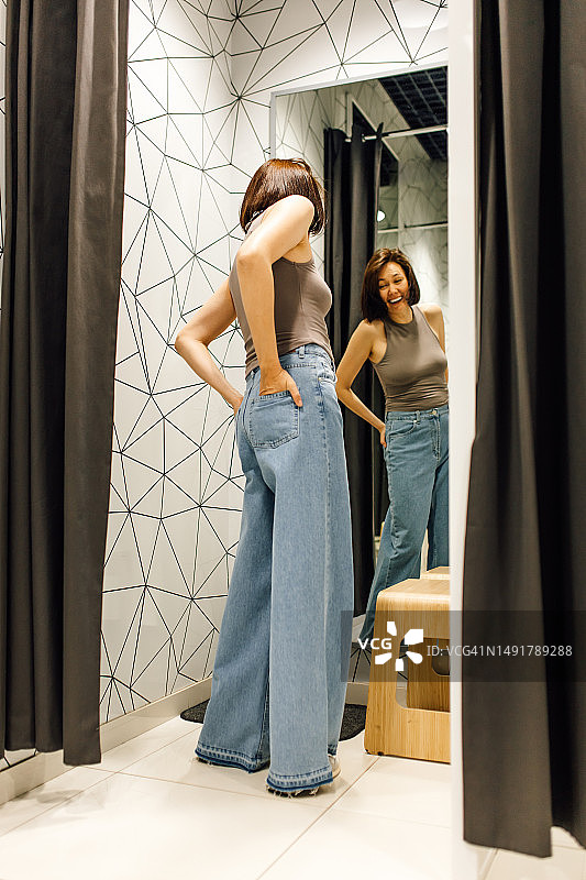 在试衣间里试穿新牛仔裤时大笑的优雅棕发中年妇女图片素材