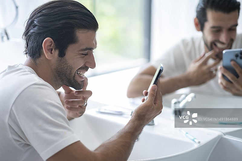 在浴室水槽前看手机的男人图片素材