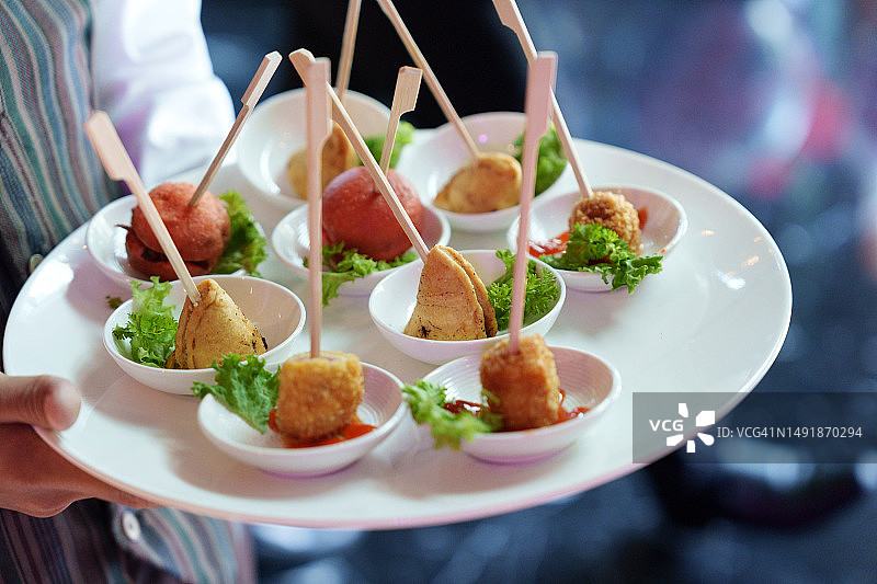 在喜庆活动、聚会或婚礼招待会上，服务员熟练地端着装满小吃的盘子图片素材