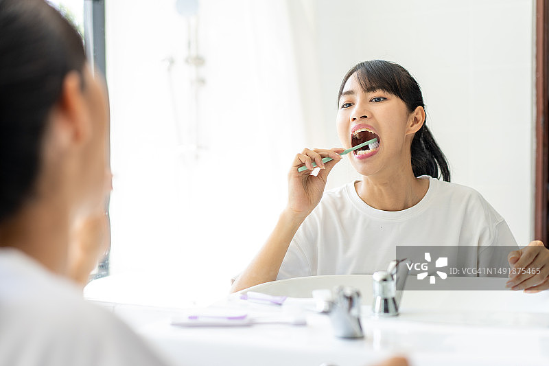 女人在家用牙刷清洁牙齿并照镜子图片素材