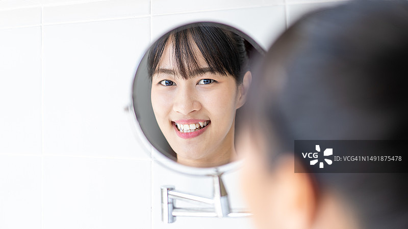 女人在家用牙刷清洁牙齿并照镜子图片素材