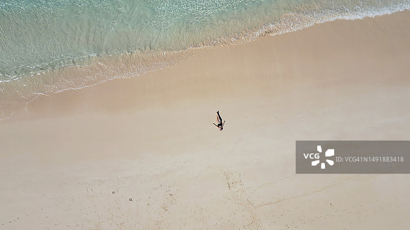 女子躺在海滩水边的鸟瞰图图片素材