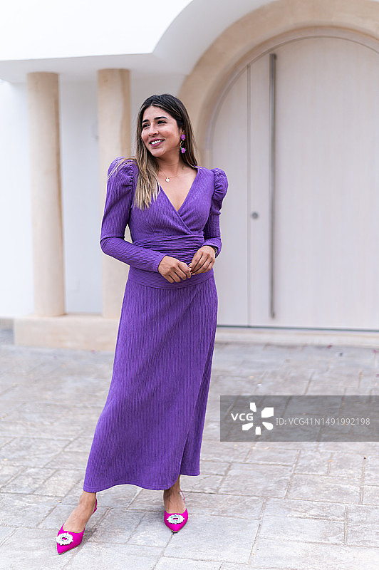 模特在建筑物外身穿优雅的紫色连衣裙摆姿势图片素材