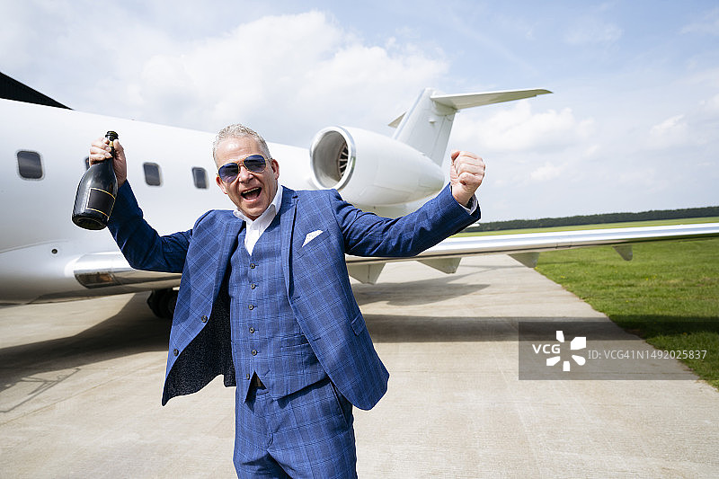 在私人飞机旁举着香槟的快乐男旅行者图片素材