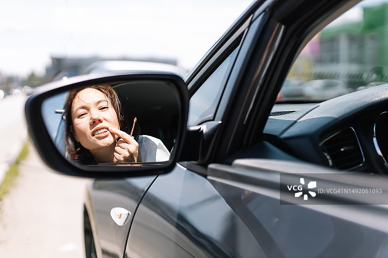 黑色汽车侧面，后视镜中迷人女子正在补妆图片素材