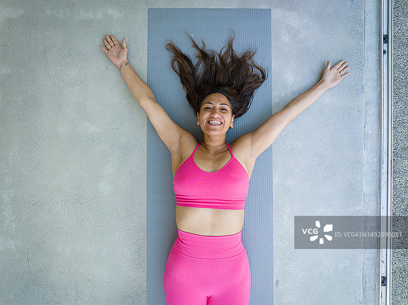 穿着粉色运动服，长发散开，像海星一样躺在瑜伽垫上的女人图片素材