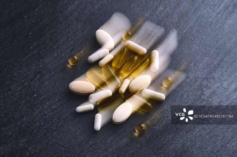 深色桌面上模糊的药丸、维生素和膳食补充剂照片图片素材