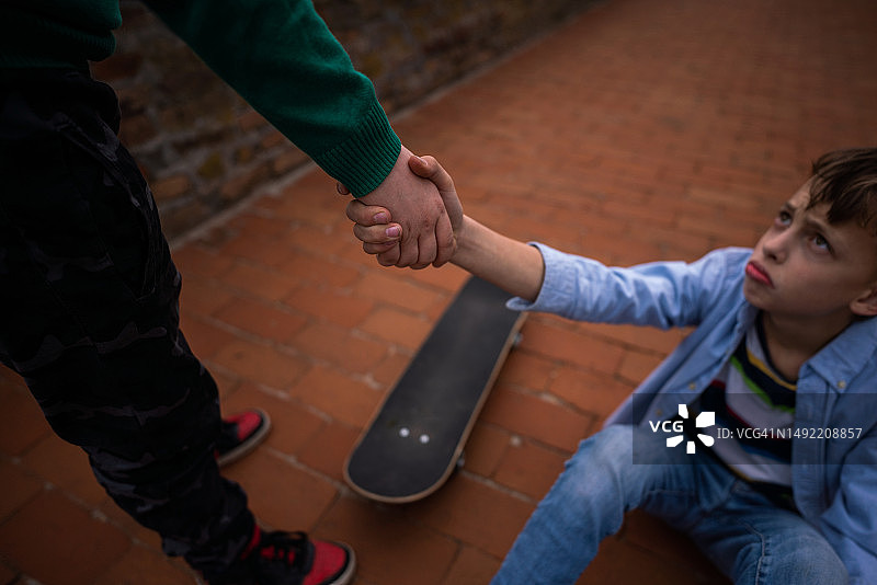 男孩帮助从滑板上摔下来的朋友图片素材