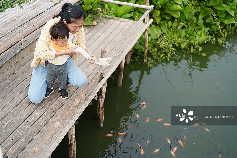 亚洲母亲和可爱男婴在花园喂鱼图片素材