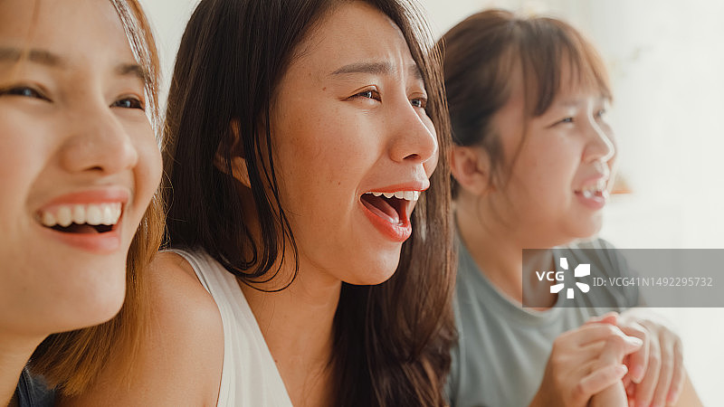 亚洲女性朋友在沙发上看喜剧频道电影或情景喜剧，通过在线视频点播观看电视的特写。休闲活动，生活方式。图片素材
