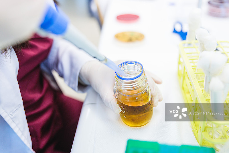 实验室内，身份不明的医疗技师用自动移液器取液体培养基样本图片素材