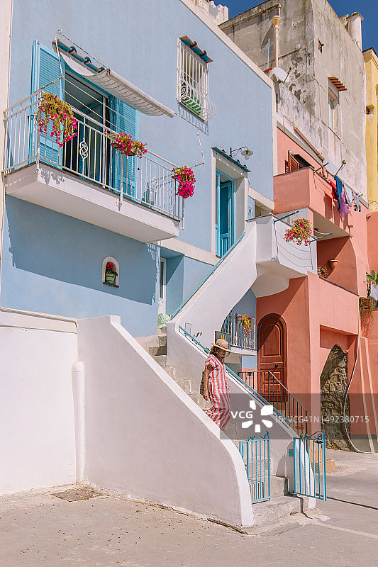 女人走下色彩鲜艳的建筑楼梯，阳台上装饰着鲜花图片素材