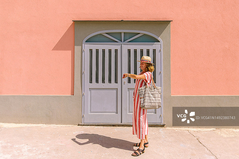 中年妇女在粉色外墙木门前看手表图片素材