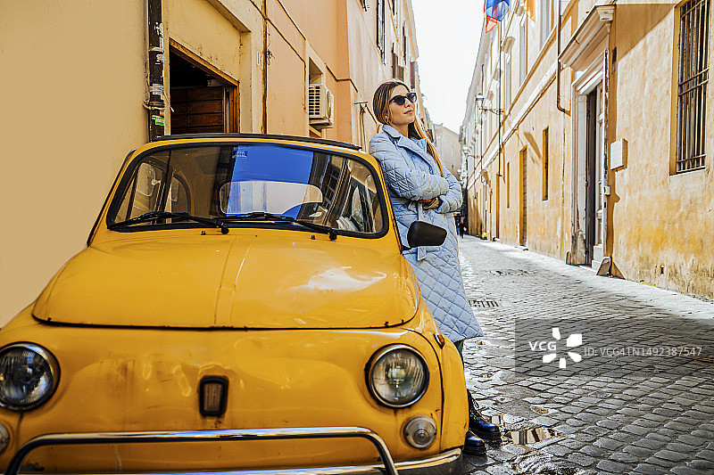 在罗马，女人靠在黄色菲亚特500复古车旁图片素材