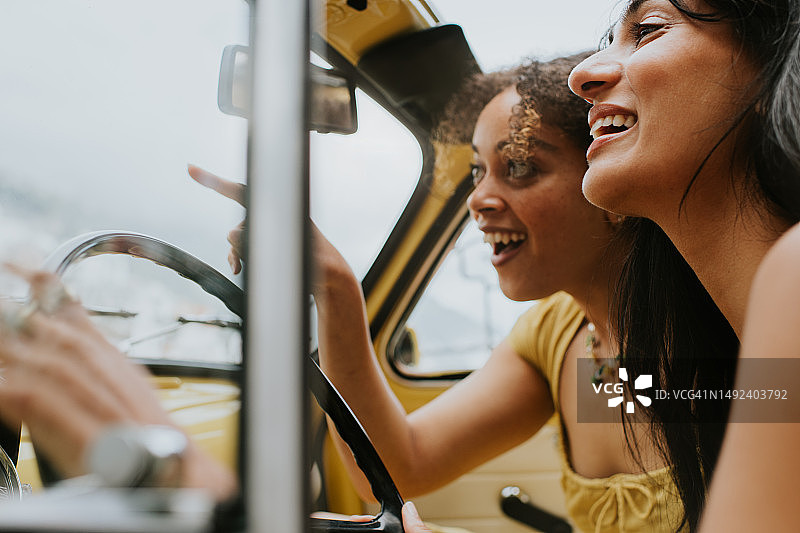 两名女子驾驶黄色复古敞篷车，焦点在前方的驾驶员图片素材
