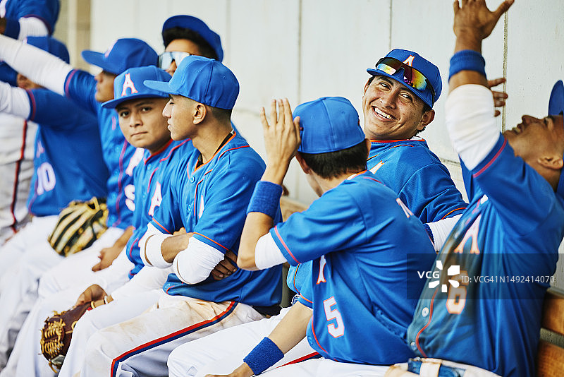 比赛期间坐在休息区里微笑的棒球队员的广角镜头图片素材