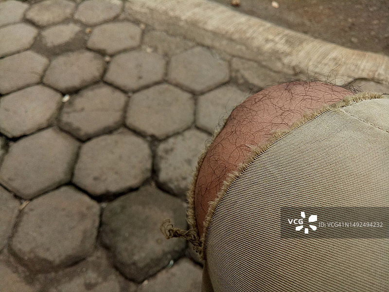 男孩穿着撕裂的棕色裤子的腿，背景是六角形砖地板图片素材