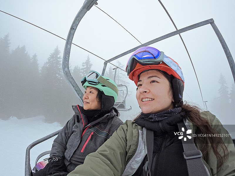 亚洲老年母亲和欧亚混血女儿乘坐滑雪缆车，肖像照图片素材