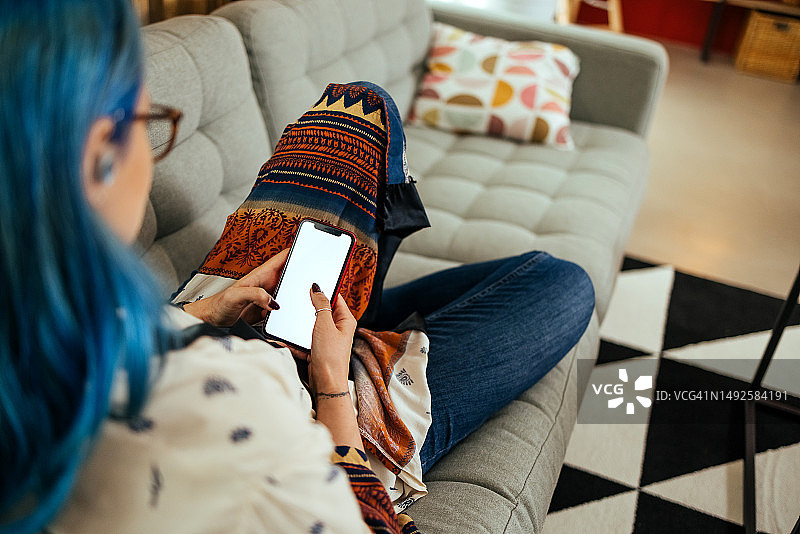 快乐的年轻女人在沙发上使用手机。图片素材