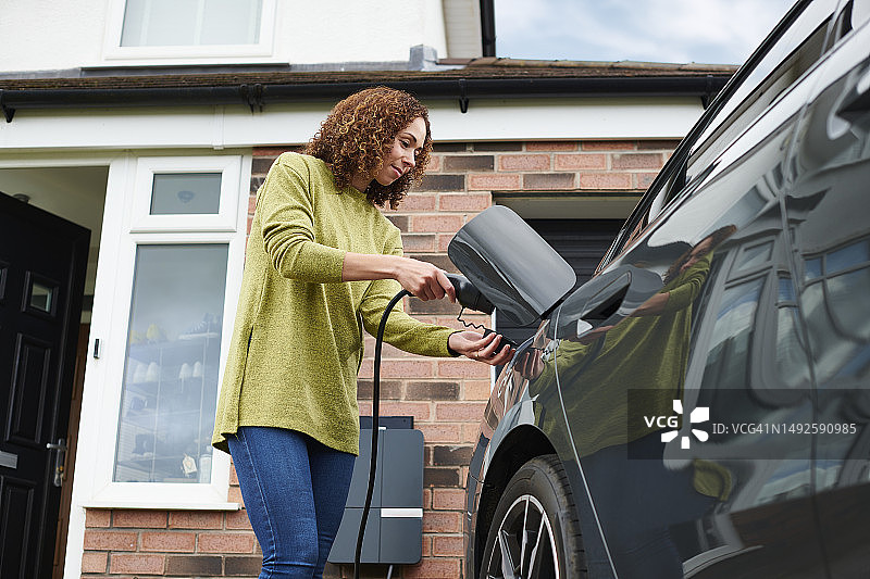 户主在车道上为电动汽车充电图片素材