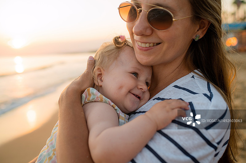 母亲和她的女婴在海边日落时度假图片素材