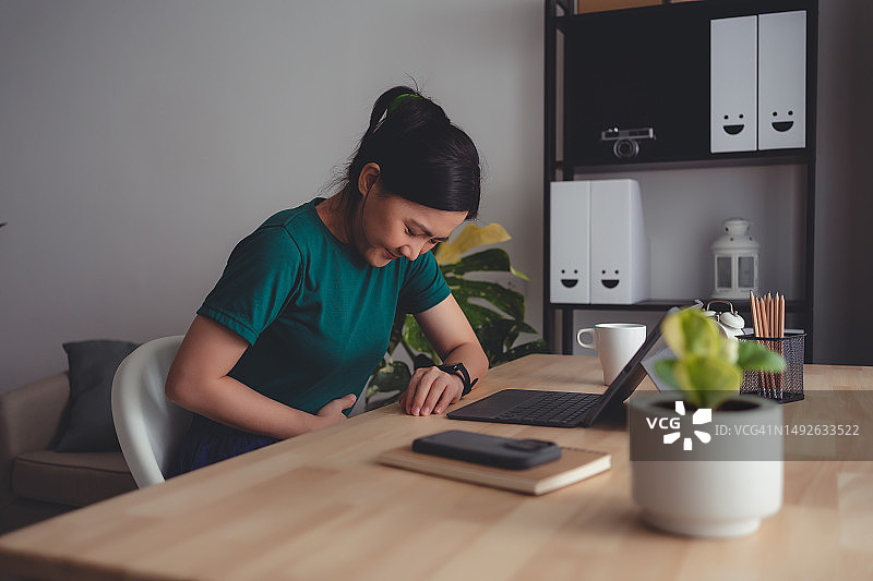 在家居办公室感到胃痛的亚洲女人图片素材