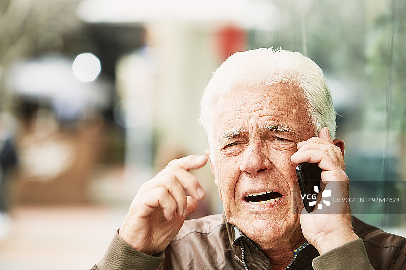 在城市街道上使用手机的沮丧老年男人图片素材