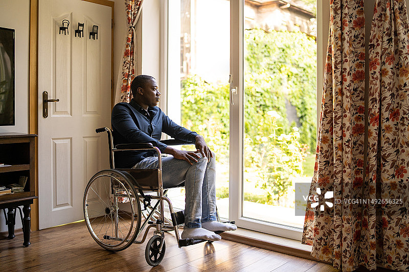 一个忧郁的男人坐在轮椅上，凝视着敞开的门口图片素材