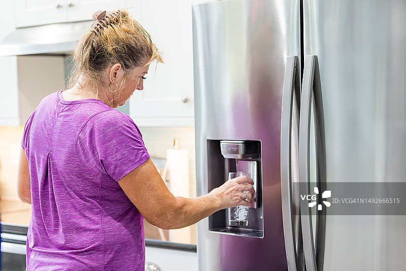 女人正在用冰箱里的过滤水倒满一个玻璃杯图片素材